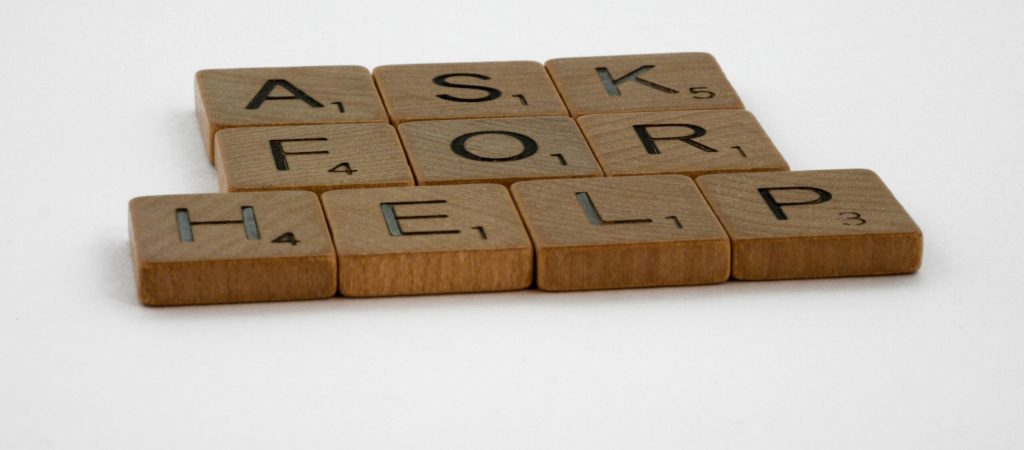 Scrabble tiles arranged on a white background forming the phrase 'Ask for Help', conveying a message of communication.